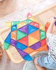 Child playing with colorful tiles from the Rainbow Shape Expansion Pack 36 pc on a table, fostering creativity.