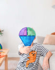 Child holding a colorful piece from the Rainbow Shape Expansion Pack 36 pc while playing on a cozy sofa.
