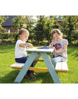 Children enjoying outdoor playtime at a picnic bench, crafting and drawing in a sunny garden.