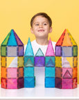 Child smiling behind a colorful castle made with Glitter Castle Pack 48 pc, showcasing imaginative play and creativity.