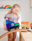 A child playing with the Rainbow Transport Pack 50 pc, building a colorful truck on a wooden track.