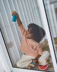 Child joyfully using the Cleaning Set, playing with a spray bottle inside a glass door.