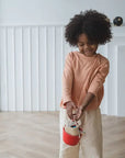 Smiling child with curly hair holding a red bucket from the Cleaning Set, ready for imaginative play.