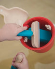Child's hands playing with wooden toys in a red bucket from the Cleaning Set.