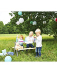 Children enjoying a picnic at the Nicki picnic bench in a sunny outdoor setting with toys and decorations.