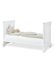 Cot bed 'Emilia' in sleek matt white finish, featuring elegant details and a cozy teddy bear for a stylish nursery.