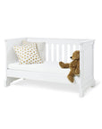 Cot Bed 'Emilia' in matte white with slatted design, decorative pillow, and teddy bear, perfect for a stylish nursery.