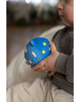 A baby holding the Night and Day Teether Ball, a soft and colorful toy designed for early movement and play.