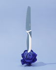 KiddiKutter Knife - Blueberry showcased with a beautiful blue rose against a soft pastel background.