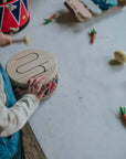 Child playing with a wooden Drum on a table, exploring creativity and rhythm with playful accessories.
