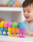 A child joyfully playing with Rainbow Wooden Eggs arranged in colorful cups on a table.