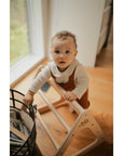 Toddler exploring with a wooden Pikler Triangle climbing frame in a cozy indoor setting.