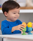 Child playing with Rainbow Wooden Eggs, stacking colorful wooden eggs on green stands in a bright playroom.