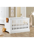 Elegant white cot bed 'Emilia' in a stylish nursery with decorative elements and adjustable height.