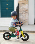 A child riding the Micro Balance Bike Peacock Green while wearing a helmet and protective gear.