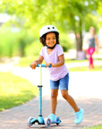 A happy child riding the Mini Micro Deluxe scooter with a helmet, enjoying a sunny day outdoors.