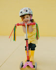 Child riding the Mini Micro Deluxe scooter with a colorful helmet and playful outfit against a bright yellow background.