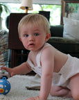 A baby playing with the Night and Day Teether Ball on a cozy rug in a bright living room.