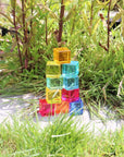 Colorful Tickit Gem Cubes stacked in grass, showcasing their transparency and light-catching brilliance.