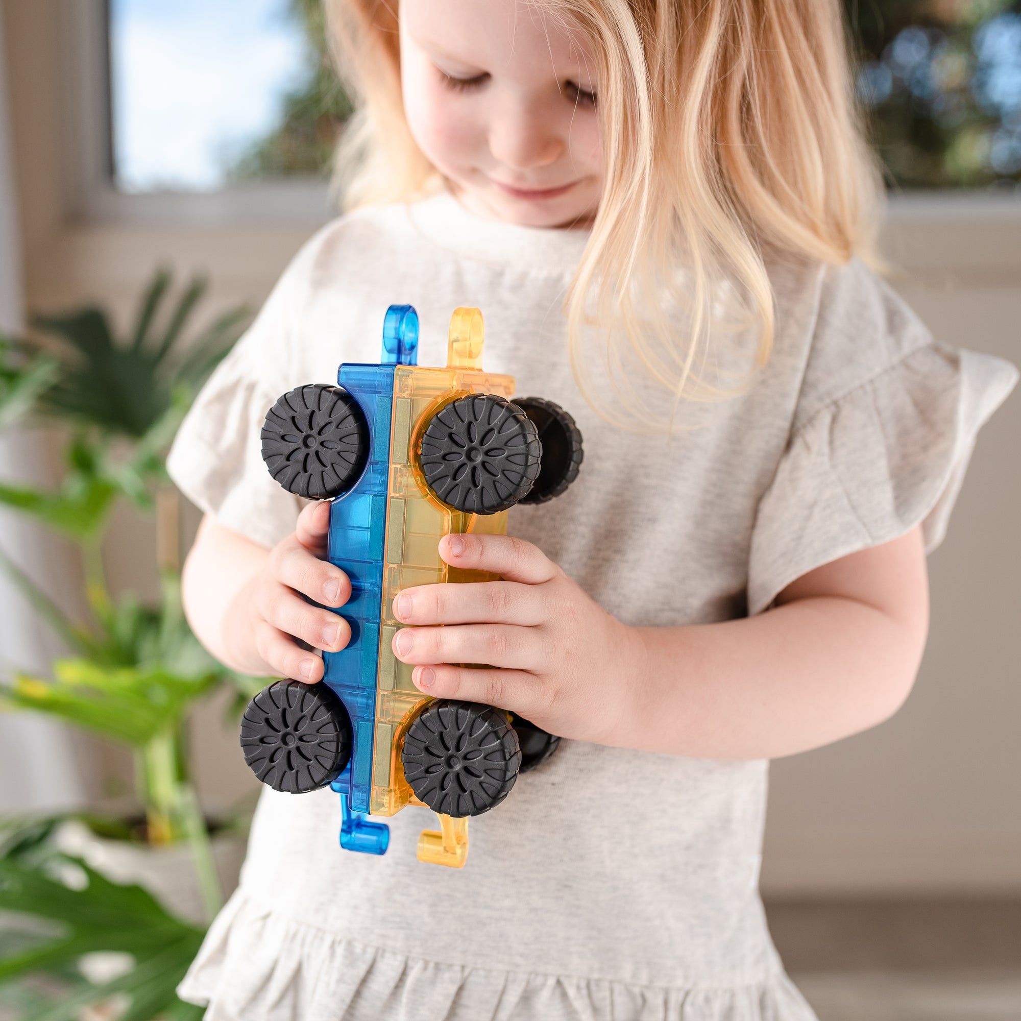 Child holding a toy train made of interlocking blocks in a home setting