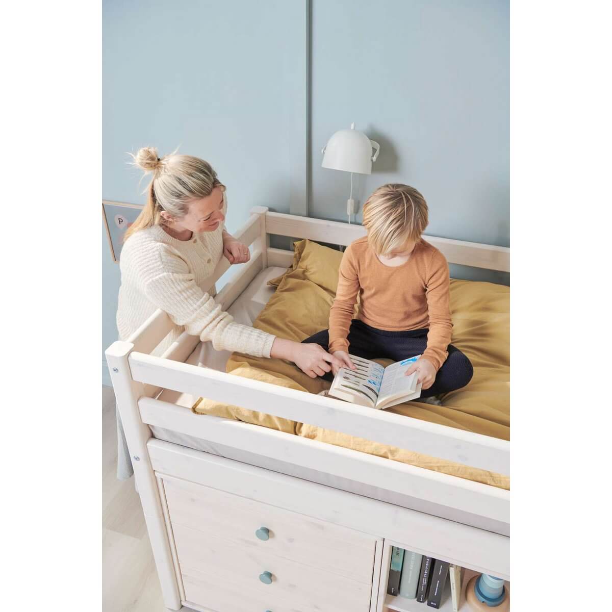 A mother reading with her child on a high bed, featuring safety rail and storage underneath, in a cozy bedroom setting.