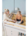 A mother reading with her child on a high bed, featuring safety rail and storage underneath, in a cozy bedroom setting.