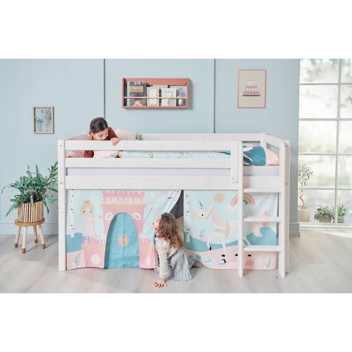 Two children playing with a high bed featuring a safety rail and colorful themed curtains, in a bright room.