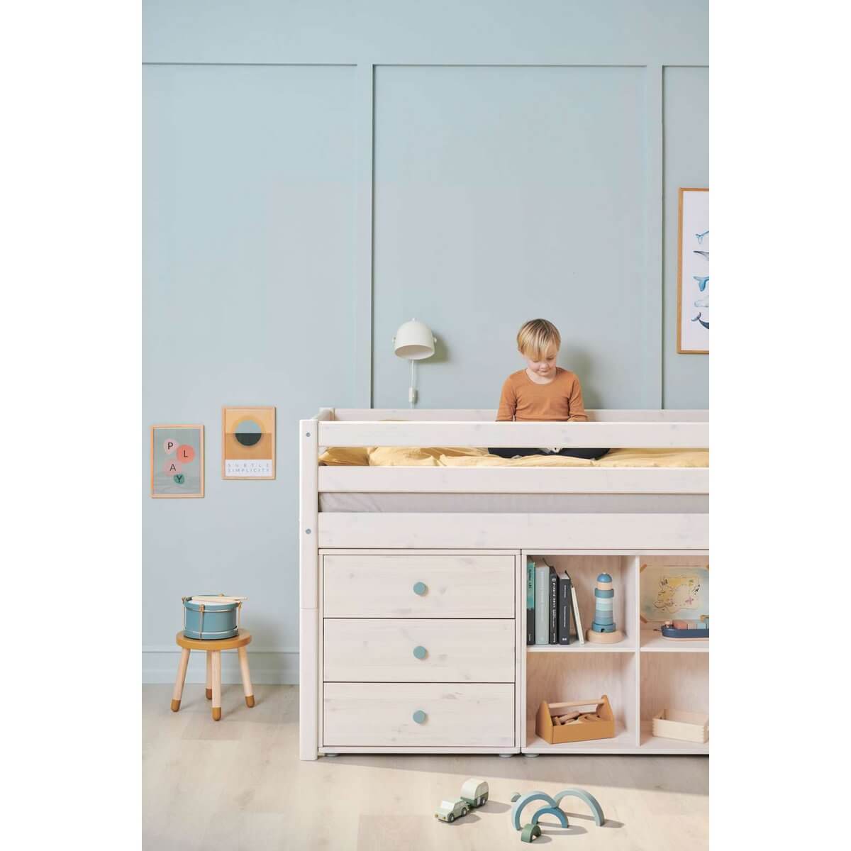 Child sitting on a high bed with safety rail and storage underneath, in a bright, cozy bedroom.