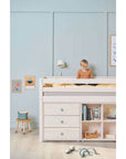 Child sitting on a high bed with safety rail and storage underneath, in a bright, cozy bedroom.