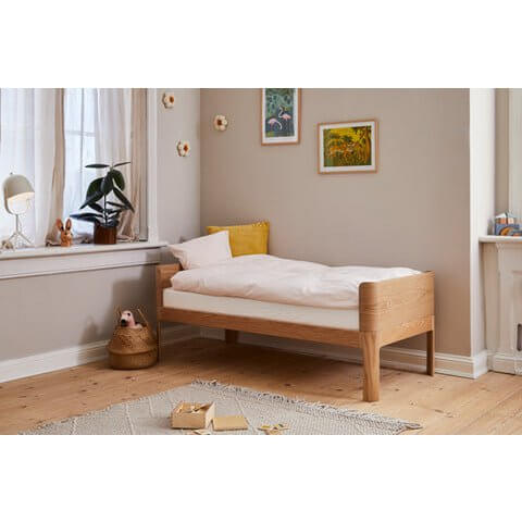 FLEXA Nova Junior Bed in oak with soft bedding in a cozy bedroom setting, featuring curved design and natural decor.