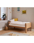 FLEXA Nova Junior Bed in oak with soft bedding in a cozy bedroom setting, featuring curved design and natural decor.