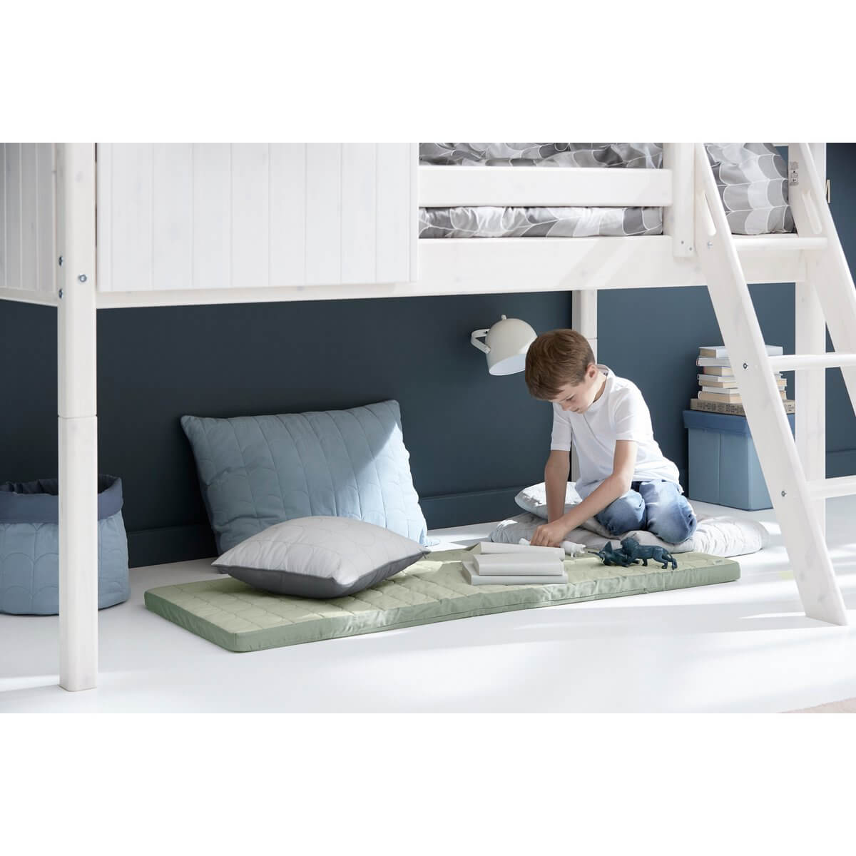 Child enjoying storytime under the high bed, surrounded by cushions and decor, creating a cozy reading nook.