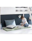 Child enjoying storytime under the high bed, surrounded by cushions and decor, creating a cozy reading nook.
