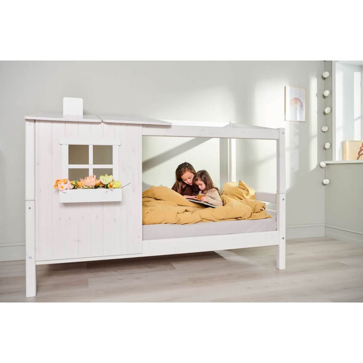 Two children snuggled in a white single bed with a half house design, creating a cozy and imaginative space.