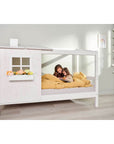Two children snuggled in a white single bed with a half house design, creating a cozy and imaginative space.