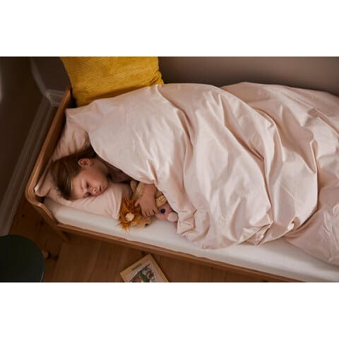 A child peacefully sleeping in a cozy junior bed with stuffed toys under soft pink bedding.