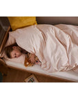 A child peacefully sleeping in a cozy junior bed with stuffed toys under soft pink bedding.