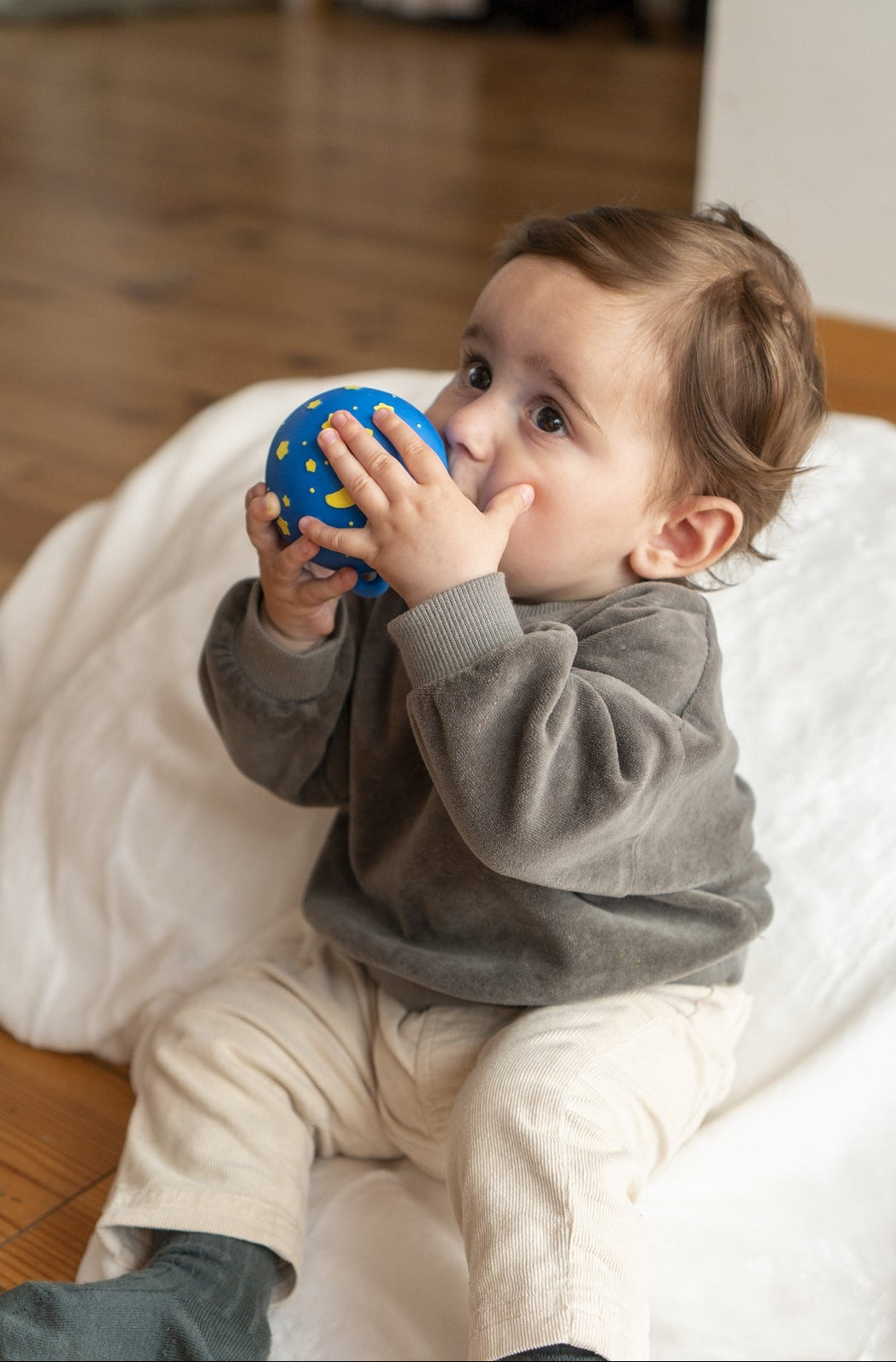 Child playing with a blue ball on a wooden floor