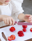 Child using KiddiKutter Knife - Cotton Candy to slice strawberries on a cutting board.