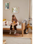 A young girl sitting on a FLEXA Nova Junior Bed, playing with toys in a cozy, well-decorated kids' room.