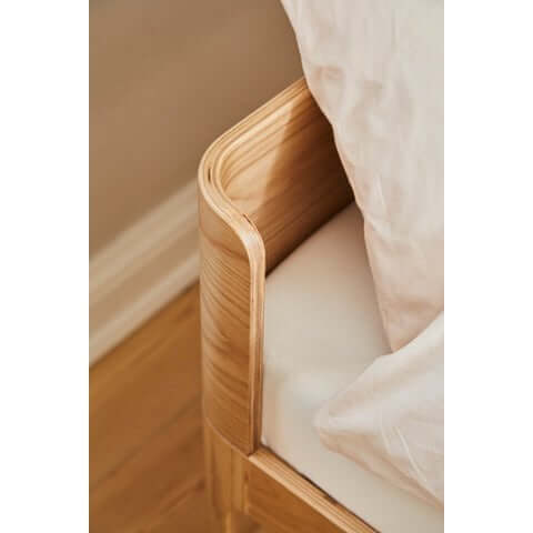 Close-up of the rounded corner of a junior bed with soft edges and natural wood finish.