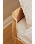 Close-up of the rounded corner of a junior bed with soft edges and natural wood finish.