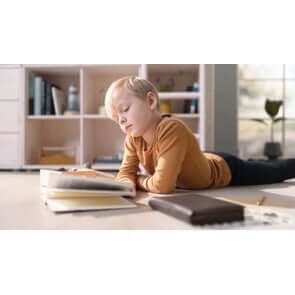 Child reading a book on the floor near a bookshelf in a cozy room setting.