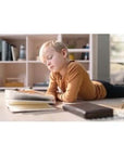 Child reading a book on the floor near a bookshelf in a cozy room setting.