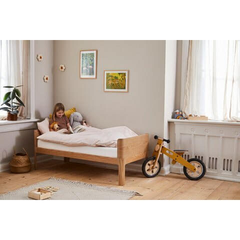 Child enjoying bedtime reading on a FLEXA Nova Junior Bed in oak, featuring a cozy design and playful decor.