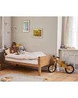 Child enjoying bedtime reading on a FLEXA Nova Junior Bed in oak, featuring a cozy design and playful decor.