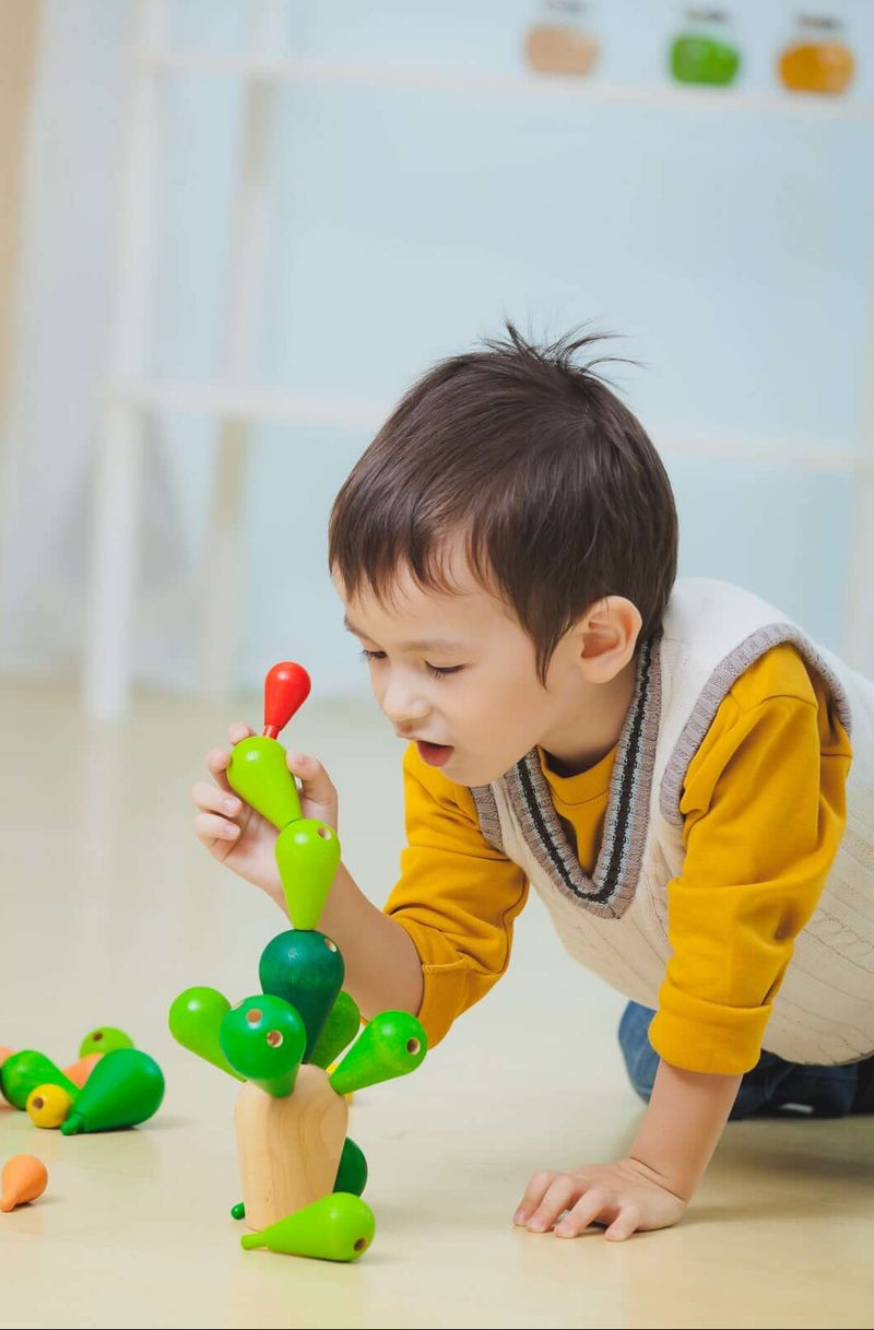 Child playing with PlanToys Balancing Cactus game, stacking colorful wooden branches carefully.