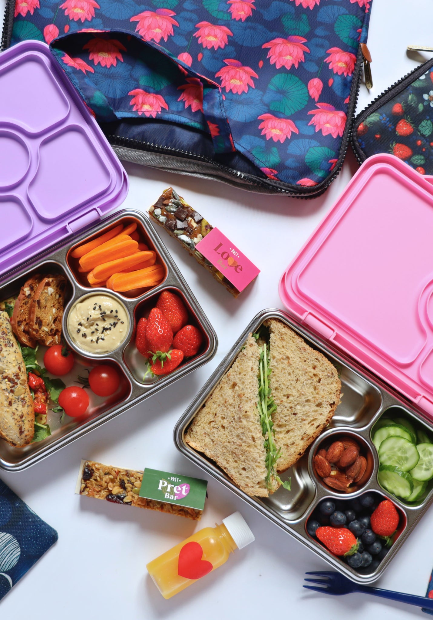 Yumbox Pret stainless steel lunch box with colorful compartments, vegetables, fruits, and snacks inside a vibrant lunch setting.
